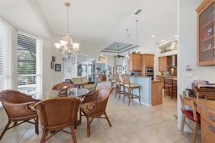 Dining room with a chandelier, ceiling fan, light tile patterned flooring, and a raised ceiling