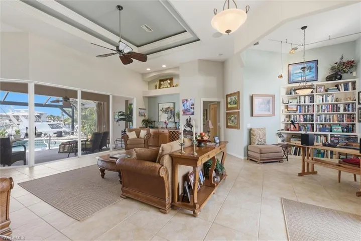 Living area with a sunroom, a tray ceiling, light tile patterned flooring, a ceiling fan, and track lighting
