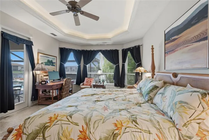 Bedroom with a ceiling fan, access to outside, a raised ceiling, light carpet, and ornamental molding