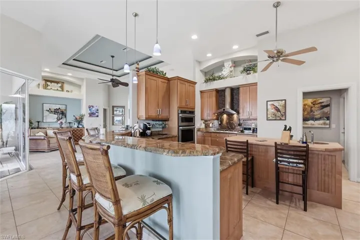Kitchen featuring a ceiling fan, a kitchen bar, a high ceiling, a peninsula, and light tile patterned flooring