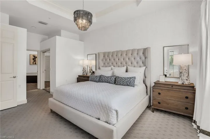 Bedroom with an inviting chandelier, light colored carpet, and a tray ceiling