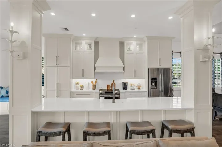 Kitchen featuring appliances with stainless steel finishes, a breakfast bar area, premium range hood, white cabinetry, and hardwood / wood-style flooring