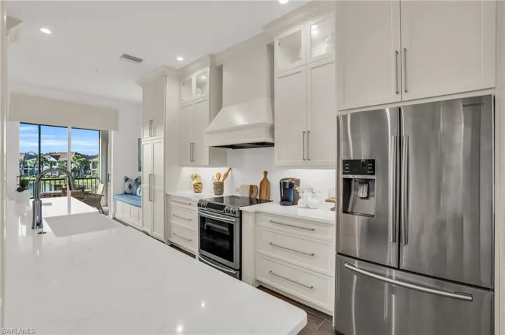 Kitchen with white cabinetry, custom exhaust hood, stainless steel appliances, sink, and light stone counters