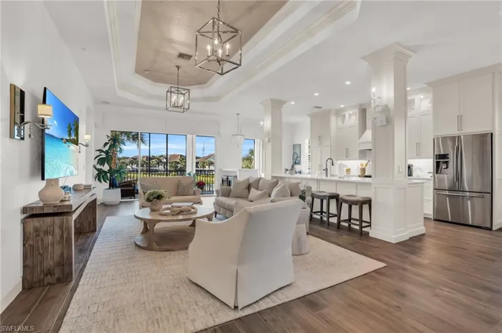 Living room with a notable chandelier, hardwood / wood-style floors, ornate columns, and a tray ceiling