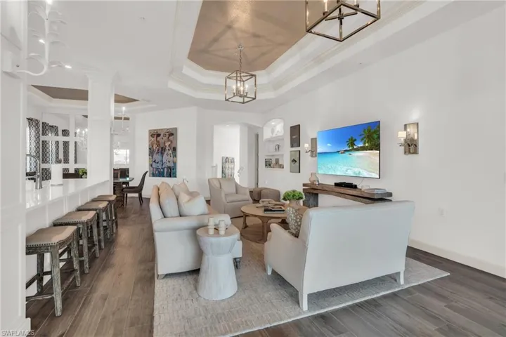 Living room with dark wood-type flooring, a raised ceiling, crown molding, and decorative columns