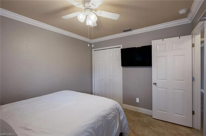 Bedroom with crown molding, ceiling fan, a closet, and light tile patterned flooring