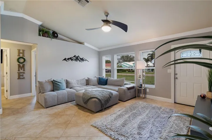 Living room with ornamental molding, vaulted ceiling, light tile patterned flooring, and ceiling fan