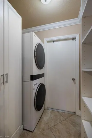 Washroom featuring a textured ceiling, estacked washer and dryer, light tile patterned floors, and ornamental molding