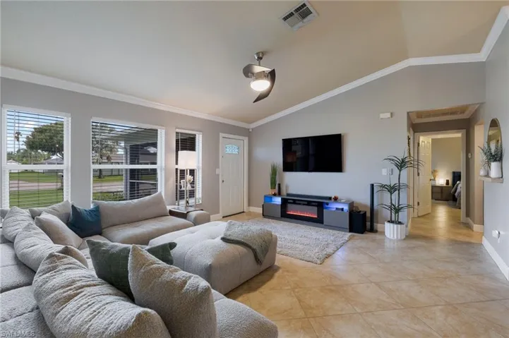 Living area featuring ornamental molding, lofted ceiling, a glass covered fireplace, and light tile patterned floors