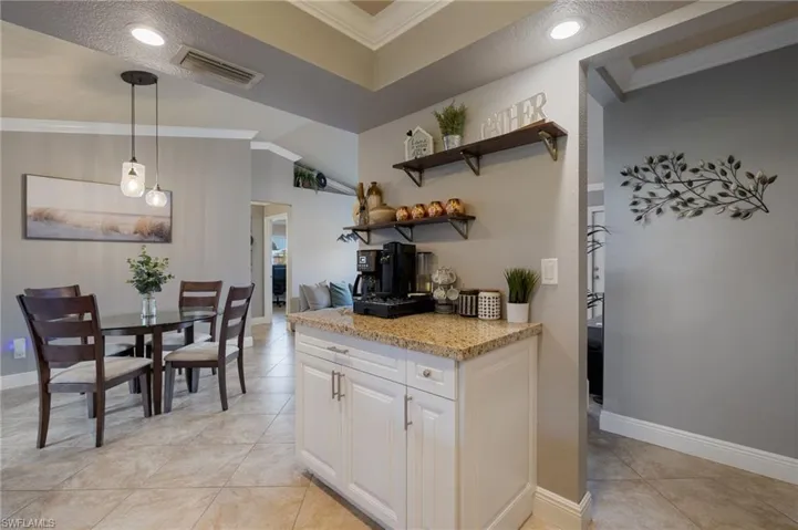 Kitchen featuring crown molding, light stone countertops, white cabinets, decorative light fixtures, and open shelves