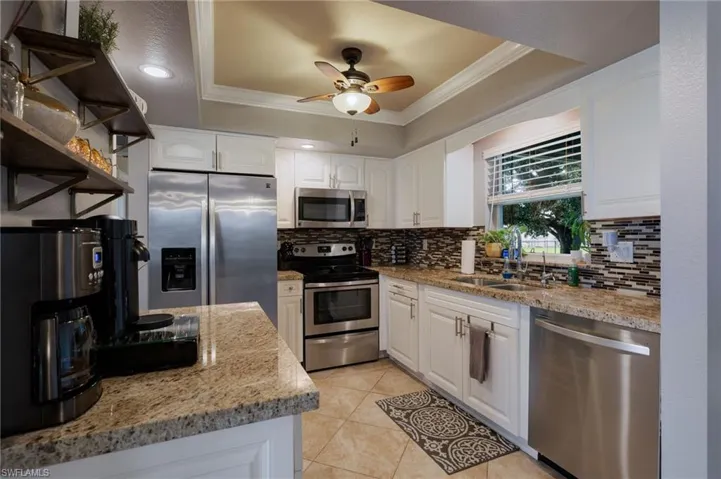Kitchen featuring a tray ceiling, white cabinetry, appliances with stainless steel finishes, light stone counters, and crown molding