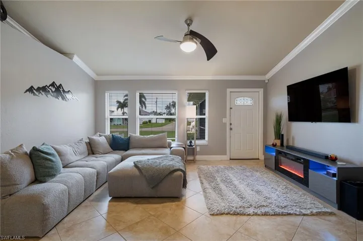 Living area with crown molding, a ceiling fan, a glass covered fireplace, and tile patterned flooring