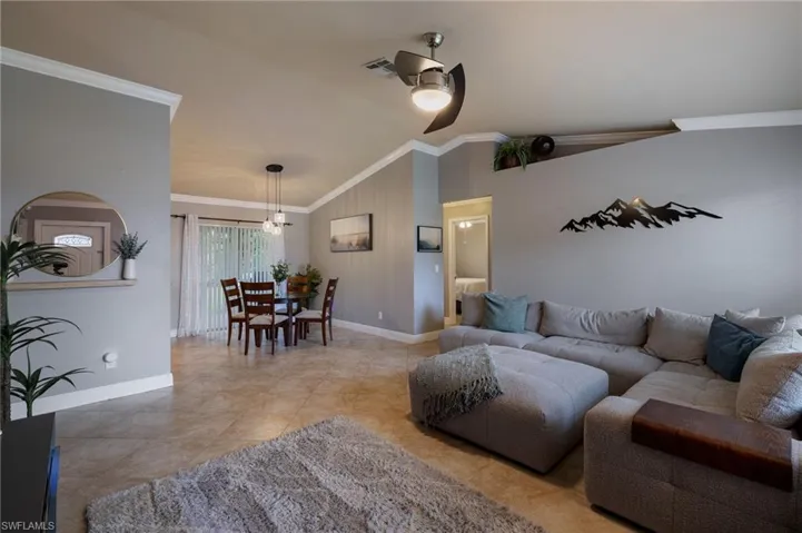 Living room featuring ornamental molding, vaulted ceiling, a ceiling fan, and light tile patterned floors