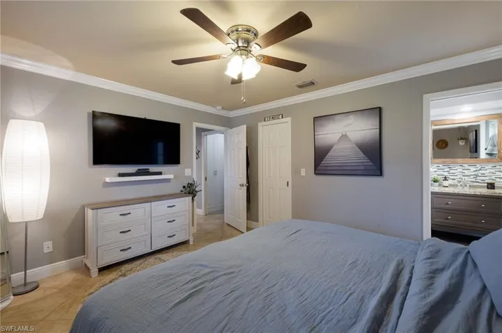 Bedroom featuring crown molding, light tile patterned floors, ceiling fan, and ensuite bathroom