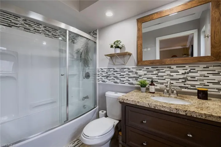 Full bath featuring combined bath / shower with glass door, backsplash, and vanity