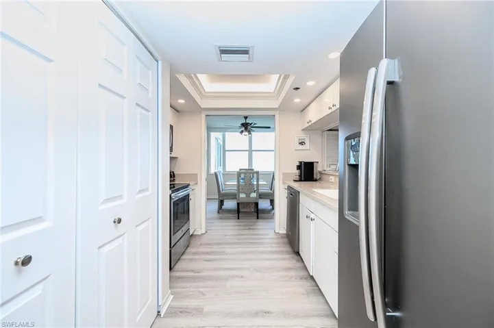Kitchen with stainless steel appliances, ceiling fan, a raised ceiling, light wood-type flooring, and white cabinets