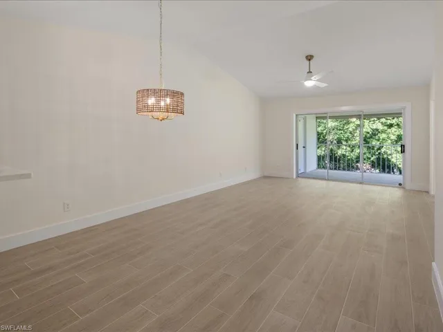 Empty room featuring high vaulted ceiling, ceiling fan with notable chandelier, and hardwood / wood-style floors