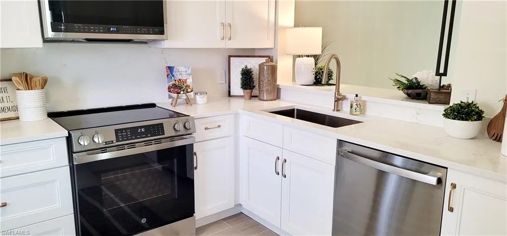 Kitchen featuring sink, light stone countertops, stainless steel appliances, and white cabinets
