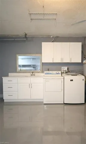 Laundry area featuring cabinet space, finished concrete floors, washer and dryer, and a textured ceiling