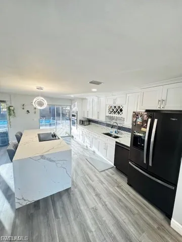 Kitchen with black appliances, light stone countertops, white cabinetry, a center island, and hanging light fixtures