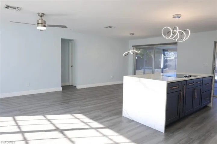 Kitchen with decorative light fixtures, open floor plan, dark wood-type flooring, and light stone counters