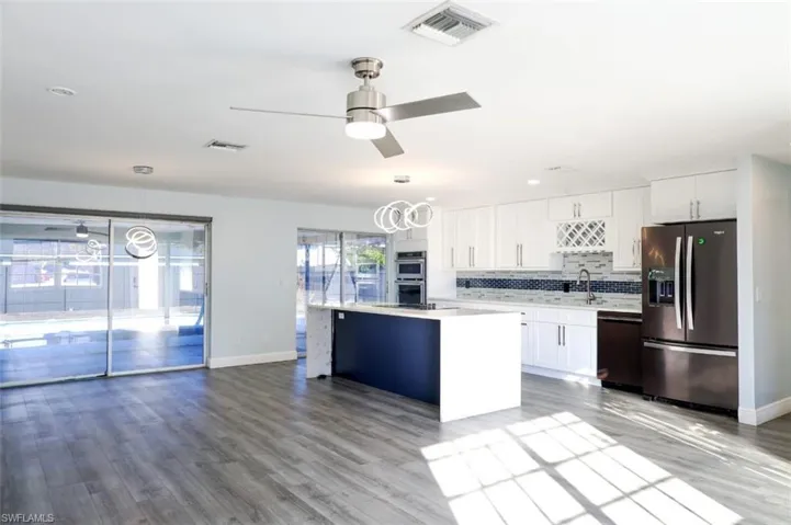 Kitchen with stainless steel appliances, white cabinets, a kitchen island, decorative light fixtures, and light wood-style flooring