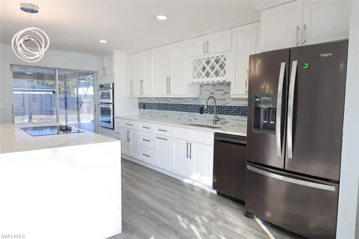 Kitchen featuring stainless steel appliances, light stone countertops, white cabinetry, and decorative light fixtures