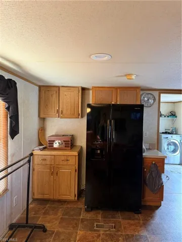 Kitchen featuring freestanding refrigerator, washer / clothes dryer, a textured ceiling, light countertops, and dark stone finish floors