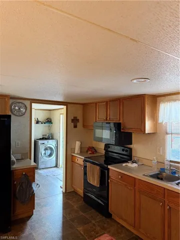 Kitchen with stove, light countertops, a textured ceiling, brown cabinetry, and fridge