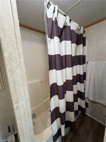 Full bath with dark wood-style flooring, a textured ceiling, shower / bath combination with curtain, and crown molding