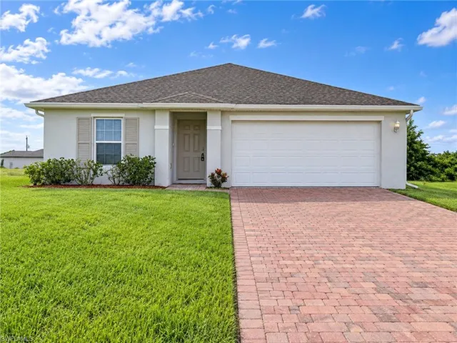 Stucco exterior with a shingle roof, paver driveway, and an attached two-car garage