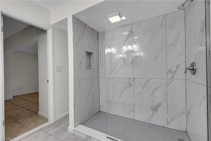 Spa like shower with upgraded large format shower tile, with built in nook and impressive glass shower wall leading to walk in shower