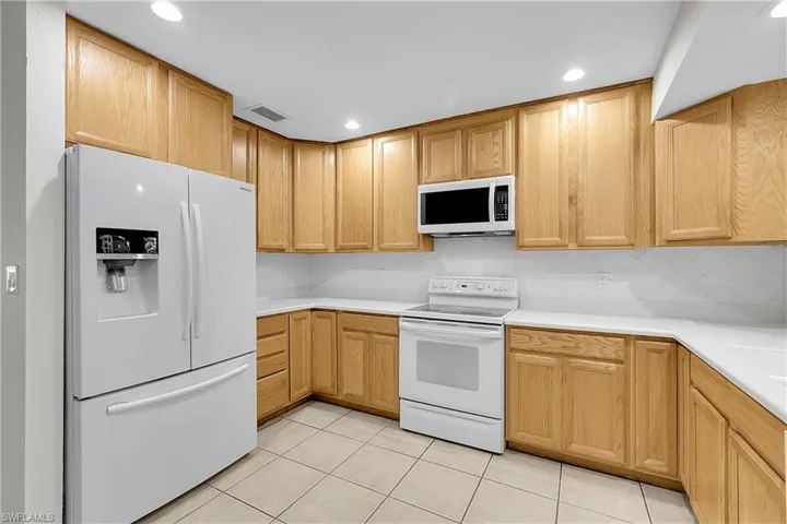 Kitchen with white appliances, recessed lighting and tile backsplash.