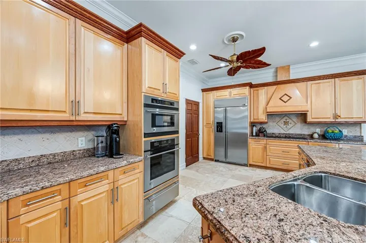 Kitchen featuring a ceiling fan, crown molding, a warming drawer, backsplash, and appliances with stainless steel finishes