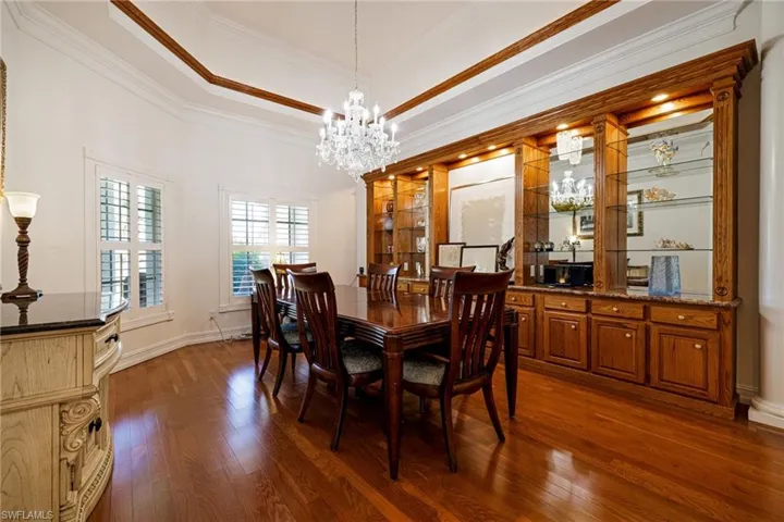 Dining space with an inviting chandelier, crown molding, a tray ceiling, and dark wood-type flooring