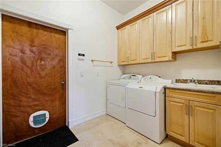 Clothes washing area with cabinet space, washer and clothes dryer, baseboards, and a sink