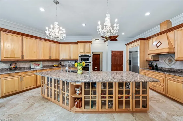 Kitchen featuring stainless steel appliances, a sink, a spacious island, a notable chandelier, and crown molding