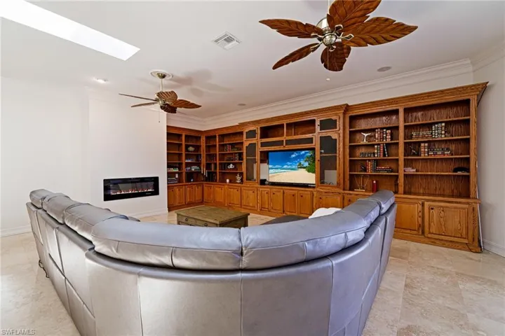 Living area with a glass covered fireplace, visible vents, ceiling fan, and crown molding