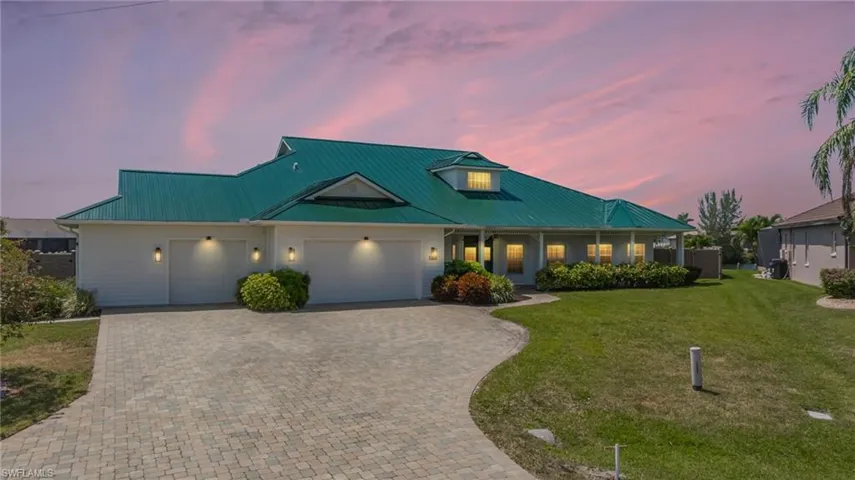 View of front of house with an attached garage, decorative driveway, a yard, and metal roof