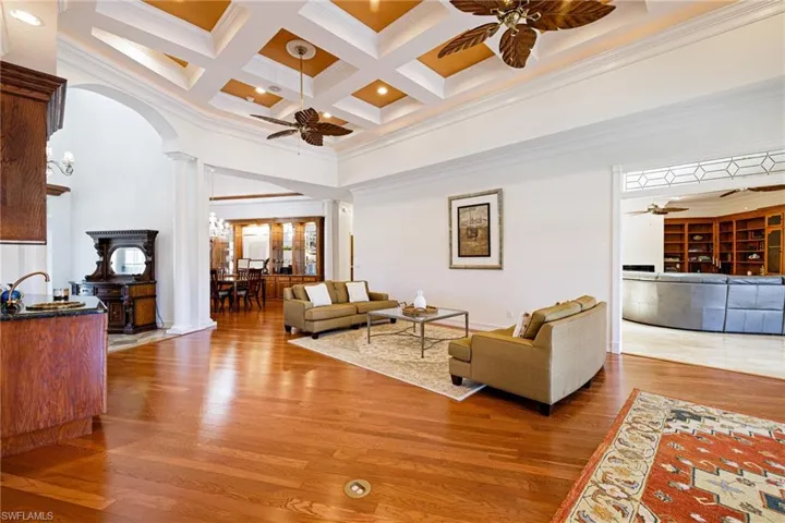 Living room with a towering ceiling, ornate columns, wood finished floors, arched walkways, and ceiling fan