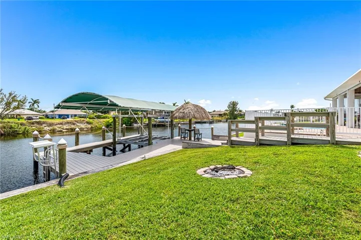 View of dock featuring an outdoor fire pit, a water view, boat lift, and a lawn