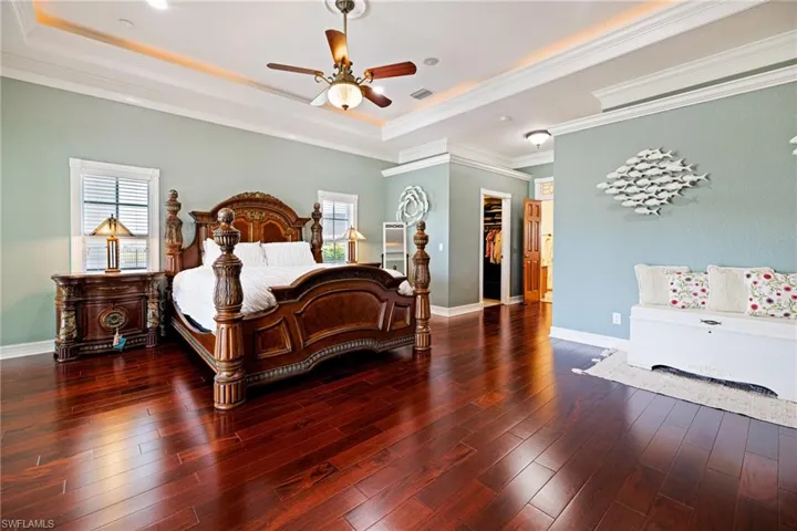 Bedroom featuring crown molding, hardwood / wood-style floors, a raised ceiling, baseboards, and visible vents