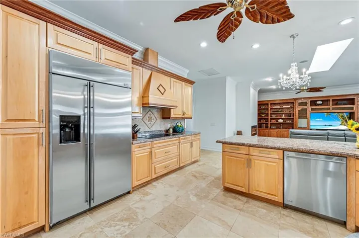 Kitchen with backsplash, ceiling fan with notable chandelier, a skylight, appliances with stainless steel finishes, and custom range hood