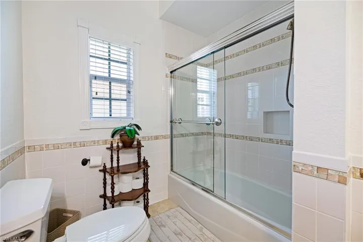 3rd Bathroom with tile walls, a wainscoted wall, enclosed tub / shower combo, and toilet