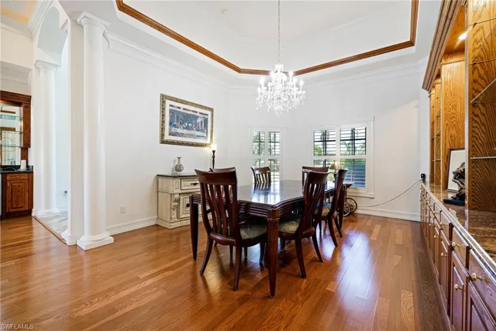 Dining space with a raised ceiling, wood finished floors, crown molding, decorative columns, and a chandelier