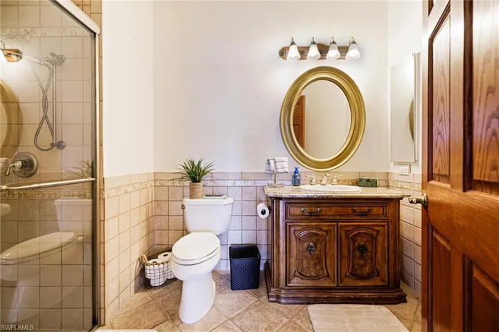 Full bathroom with a shower stall, wainscoting, vanity, tile walls, and toilet