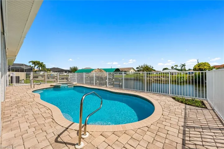 View of swimming pool with a patio area, a pool with connected hot tub, a fenced backyard, and a water view