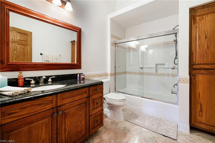 2nd Primary Bathroom featuring enclosed tub / shower combo, toilet, vanity, and marble finish floor