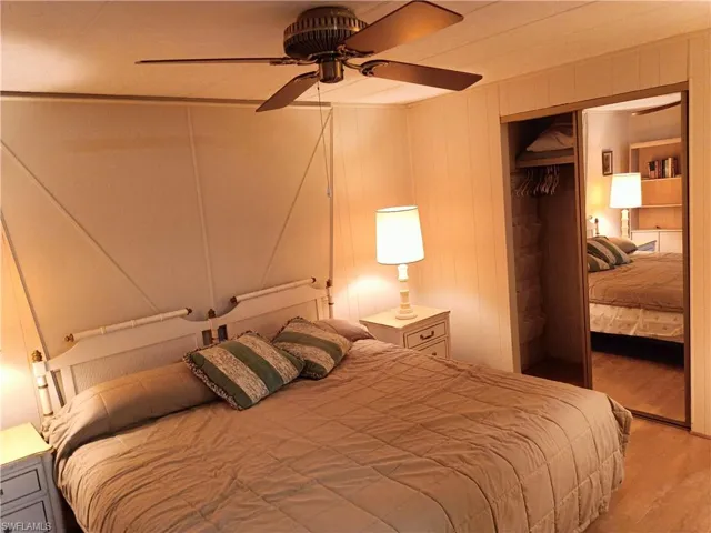 Bedroom with a closet, ceiling fan, hardwood / wood-style floors, and wooden walls