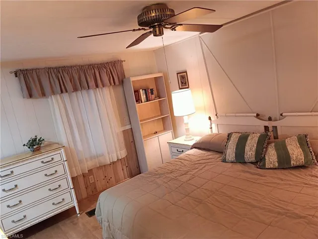 Bedroom featuring ceiling fan, wood-type flooring, and wooden walls